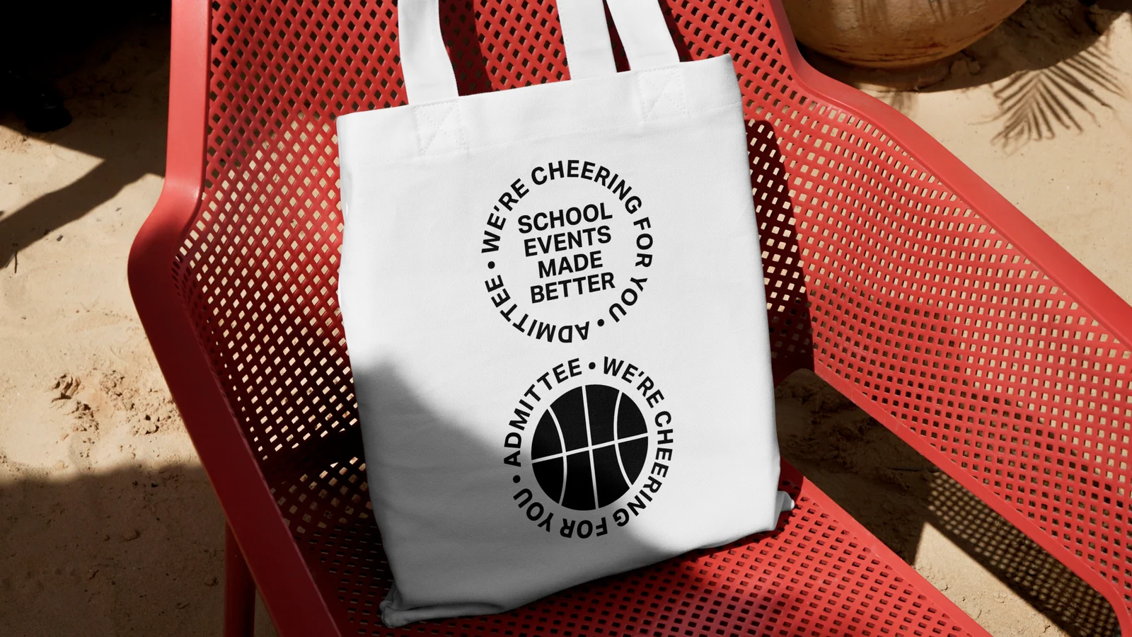 A white Admittee tote bag on a red chair, printed with “School events made better” and a basketball badge.