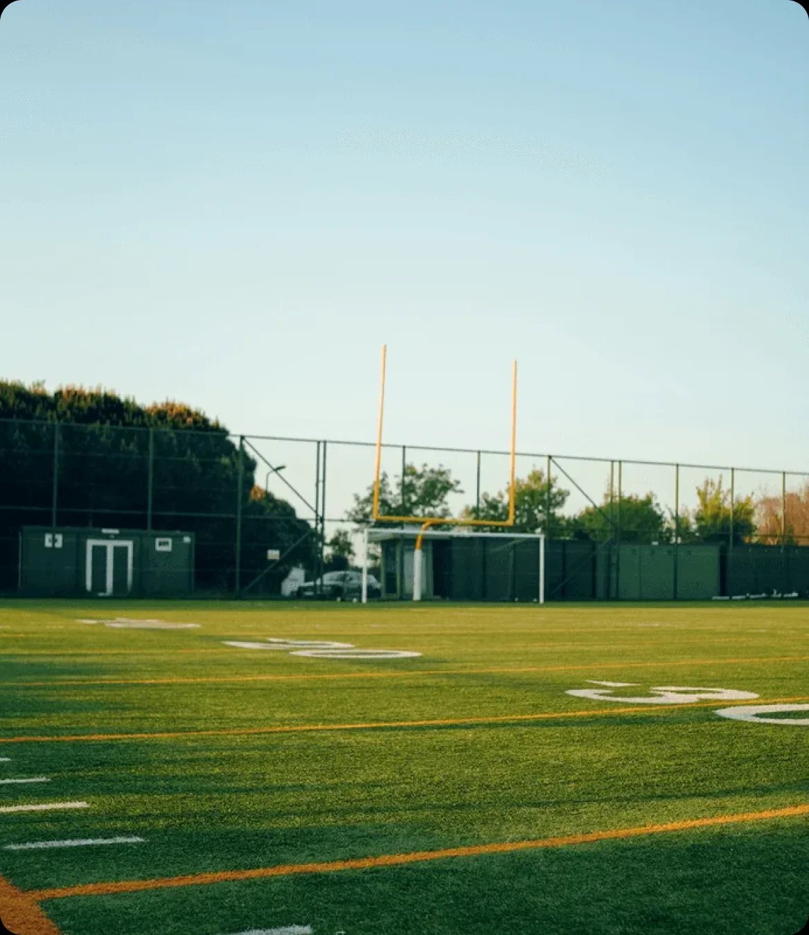 A school football field at dusk, goalposts and bleachers under a clear sky.